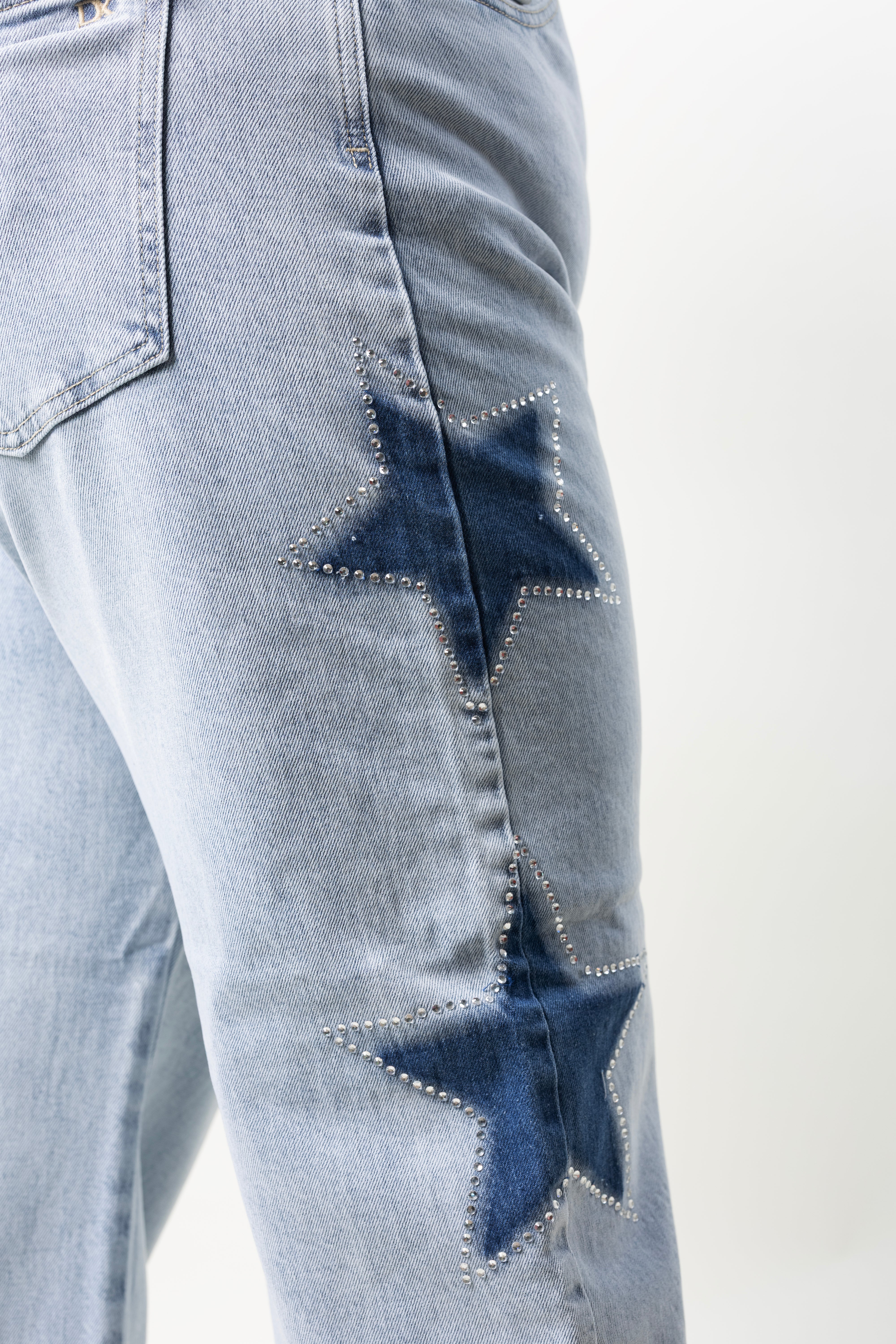 Detalle de estrellas en mezclilla con brillos sobre barrel jeans color azul claro.