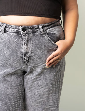 Detalle de pantalon wide leg gris con aplicación de pedrería brillante y bolsillo delantero.
