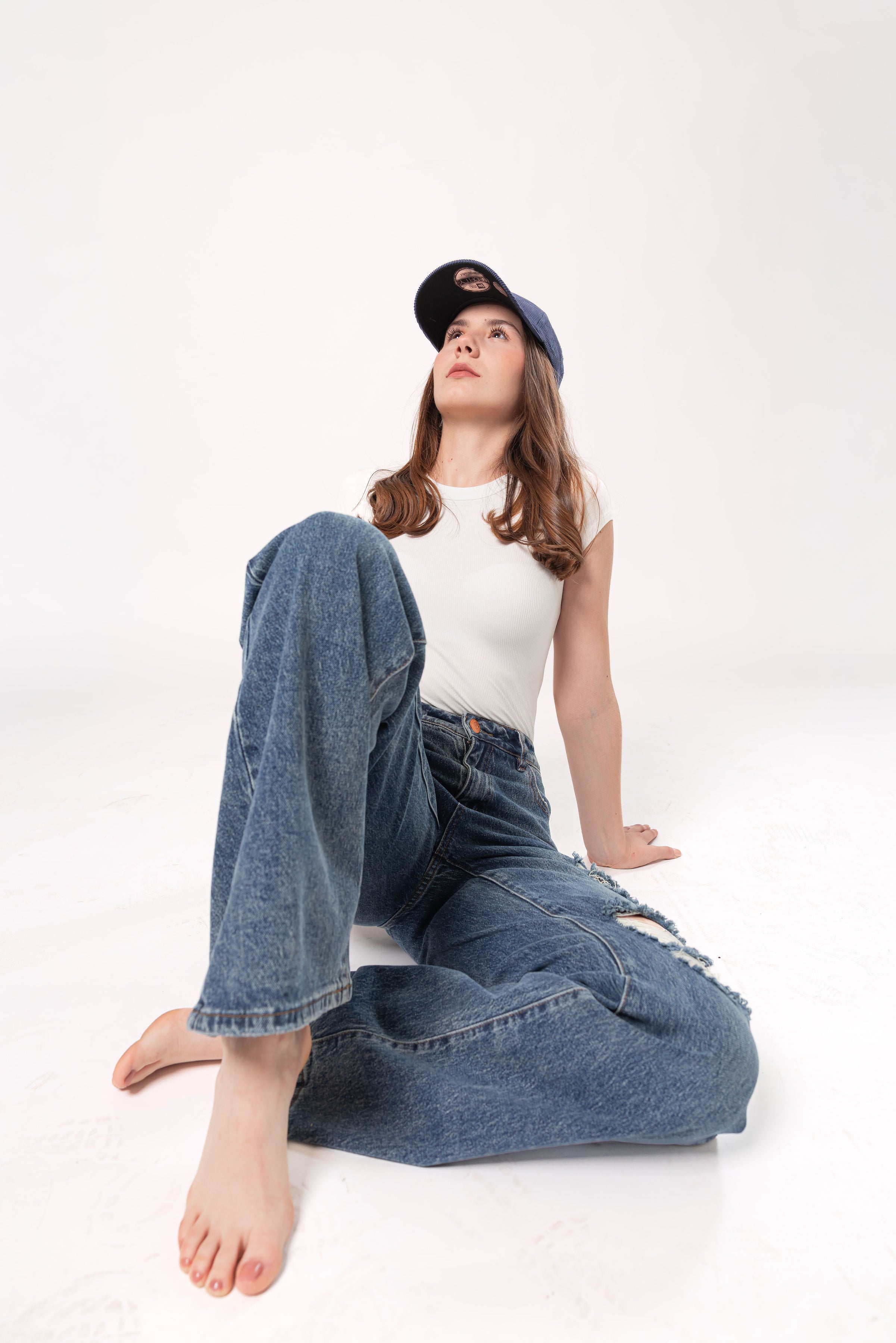 Pantalon wide leg azul con detalles destroyed en look casual femenino sentado sobre fondo blanco
