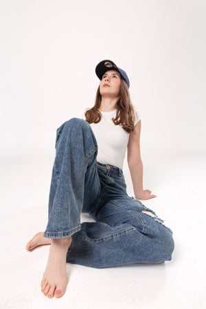 Pantalon wide leg azul con detalles destroyed en look casual femenino sentado sobre fondo blanco